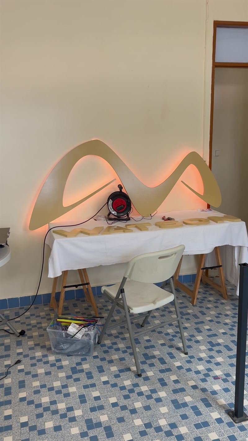 Vague lumineuse — La vague rétroéclairée au mur, avec les lettres du nom de l'entreprise